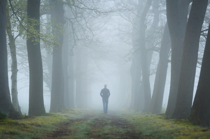Man walking in a mysterious lane on a foggy and dark morning.